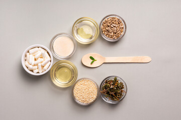 Homeopathic medicine. Homeopathic pills in a bowl and green leaves, herbs and natural products, wooden spoon from above on a light grey background. Alternative medicines top view.