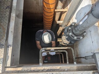 Worker Descending into a Manhole for Inspection and Maintenance, confine space. A worker wearing safety gear descends into a manhole for inspection and maintenance of underground utility systems.