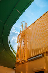 Vertical view ofFire escape stairs on buildings is constructed with metal sheet material painted in yellow throughout with a background of a blue sky during the day.