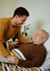 Caring young man visiting and supporting elderly man in a comforting home environment