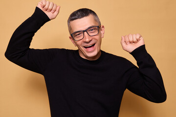 Caucasian man wearing glasses and black raglan celebrating indoors with joyful dance and raised...