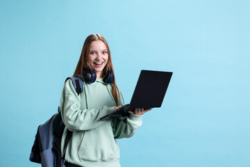Obraz premium Portrait of cheerful woman carrying laptop needed to do school homework, isolated over studio background. Joyful pupil holding notebook, preparing for university assessment
