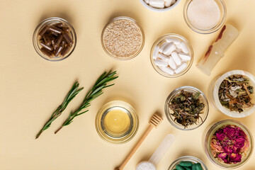 Homeopathy. Homeopathic medicines, colored pills and capsules in bowls in a beautiful composition with green leaves, herbs and various plants, on a beige background, top view. Rustic style.