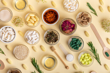 Homeopathy. Homeopathic medicines, colored pills and capsules in bowls in a beautiful composition with green leaves, herbs and various plants, on a beige background, top view. Rustic style.