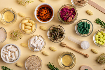 Homeopathy. Homeopathic medicines, colored pills and capsules in bowls in a beautiful composition with green leaves, herbs and various plants, on a beige background, top view. Rustic style.