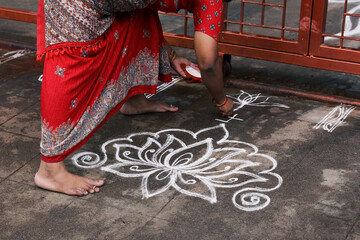 Indian women putting kolam Rangoli for Pongal front of Indian Temple dedicated to the Hindu deity of the Puranas. Dravidian vintage architecture in Tamilnadu India