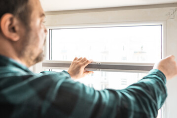 Fototapeta premium Man installs roller blinds. Handyman mesures window to fix it.