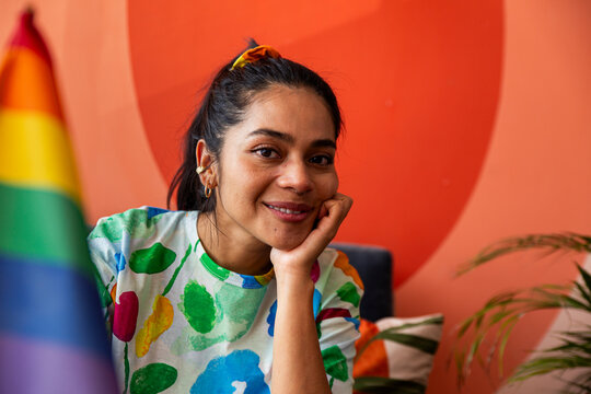 Happy woman sitting near rainbow flag in front of red wall