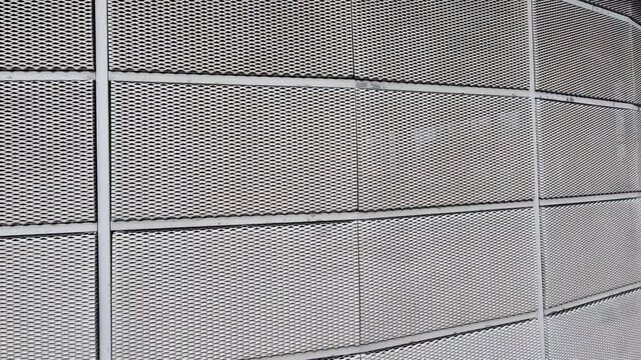 steel cladding of a building with a expanded metal lattice structure. galvanized gray nets protect the industrial building. Blue sky in contrast to a silver background, wall