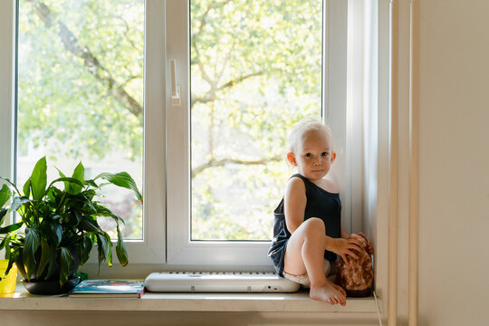 Cute boy spending leisure time sitting near window at home