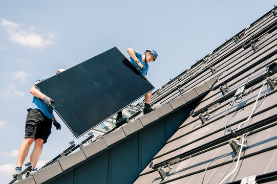 Engineers installing solar panel on roof under sky on sunny day