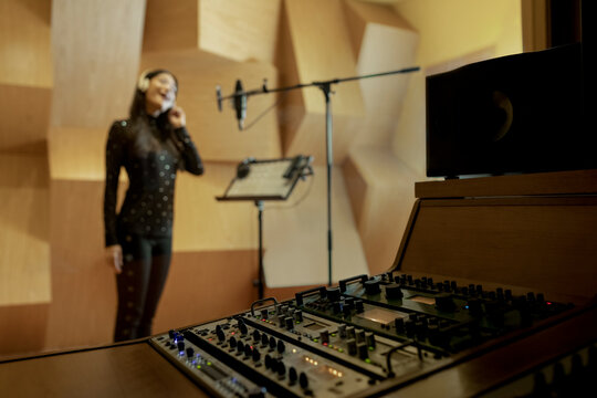 Young singer wearing wireless headphones and recording song in studio