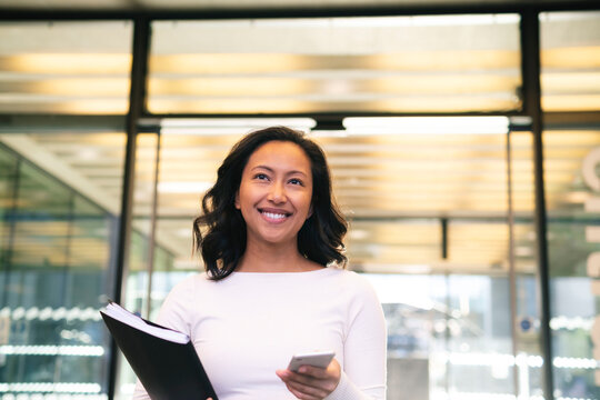 Smiling businesswoman holding documents and smart phone in office