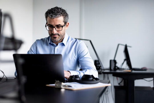 Businessman working on laptop at desk in office - Powered by Adobe