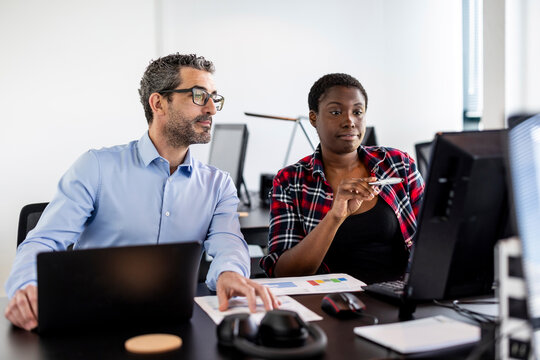 Businesswoman having discussion with colleague over computer at desk in office