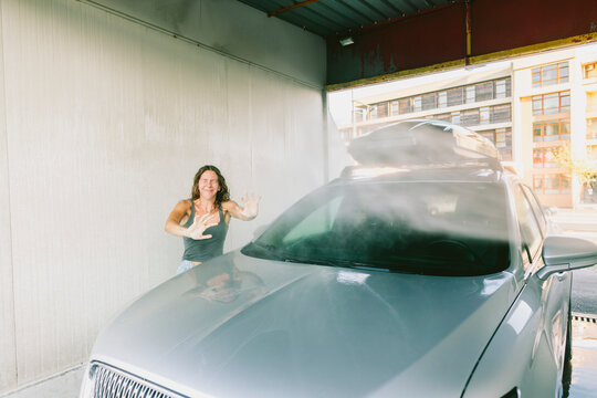 Water splashing on young woman by car at service station