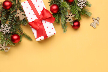 Christmas tree branches with decorations and gift box on yellow background