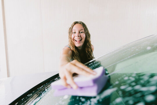 Cheerful young woman cleaning car windshield with sponge