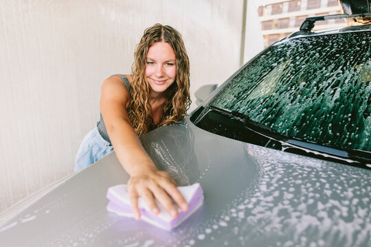 Smiling young woman cleaning car at with sponge