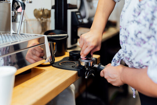 Woman tamping espresso coffee at counter in cafe