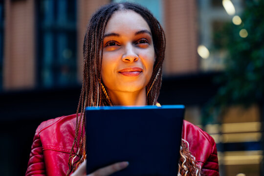 Thoughtful woman with braided hair holding tablet PC