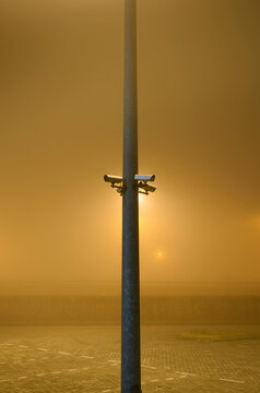 Security cameras on pole in heavy fog near sea at night