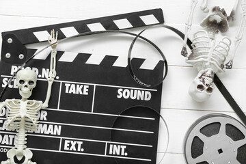 Clapperboard with film reel and skeletons on white wooden background. Halloween celebration
