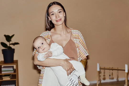 Smiling mother with amputated arm carrying baby boy and standing at home