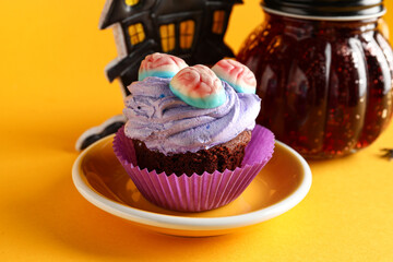 Plate with delicious Halloween cupcake and candies on orange background, closeup