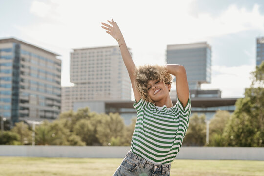 Young woman with hand raised standing at sunny day