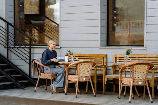 Businesswoman holding book and sitting at sidewalk cafe