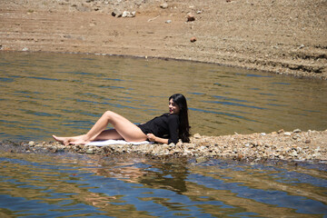 beautiful young brunette latin woman in black shirt and black bikini lying relaxed on the shore of...