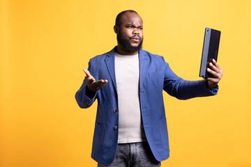 Offended man fighting with friends after receiving affronts during teleconference meeting using tablet, studio background. Rude person in disagreement with mates during videocall on portable device