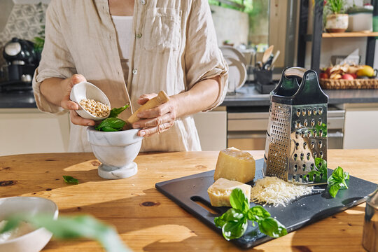 Woman adding pine nuts in mortar with basil leaves