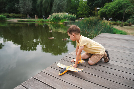Boy with toy plane looking into lake at park