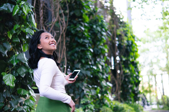 Happy woman holding smart phone and spending leisure time near plants
