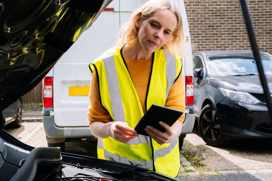 Blond insurance agent with tablet PC checking car engine