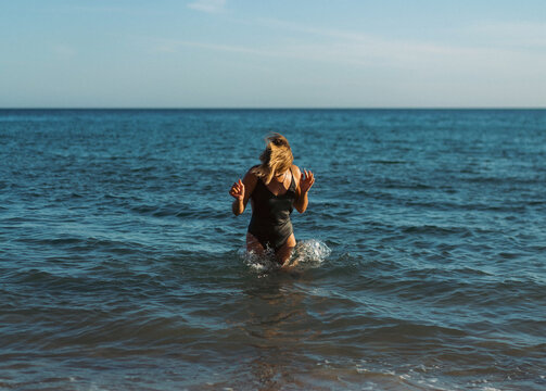 A woman stands in the sea in a swimsuit.