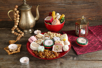 Diya lamps with candles, beads, teapot and plate of different treats on brown wooden background. Divaly celebration