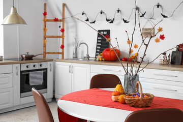 Dining table with vase, Halloween pumpkins and candies in festive kitchen