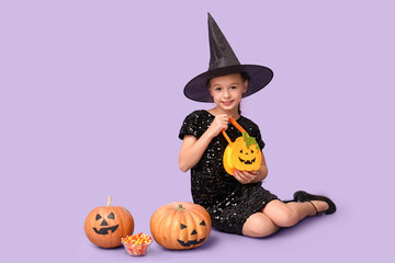 Cute little girl dressed for Halloween as witch with pumpkins, bag and candies sitting on purple background