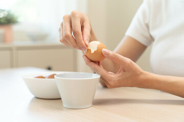 Close-up shot of woman hands peeling shell of boiled egg on the table.