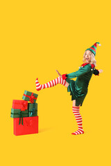 Happy young woman dressed as elf with Christmas gifts on yellow background