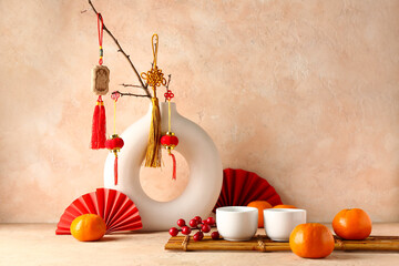 Vase with oriental symbols, cups and mandarins on table against beige grunge background. New Year celebration