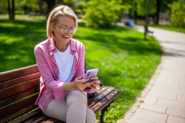 Portrait of mature woman in park. She is messaging on smartphone.