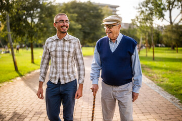 Happy grandfather and grandson are walking and talking in park.