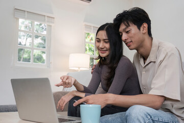 Young Couple Relaxing Together on Sofa, Enjoying Leisure Time at Home with Laptop and Coffee Mug in Cozy Living Room