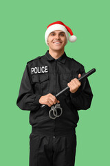 Male police officer in Santa hat with handcuffs and baton on green background