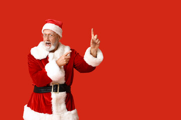 Shocked Santa Claus in glasses pointing at something on red background