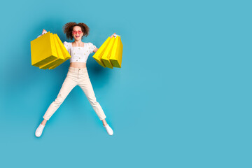 Full size photo of pretty young girl shopping bags sunglass heart shape jumping wear trendy white outfit isolated on blue color background